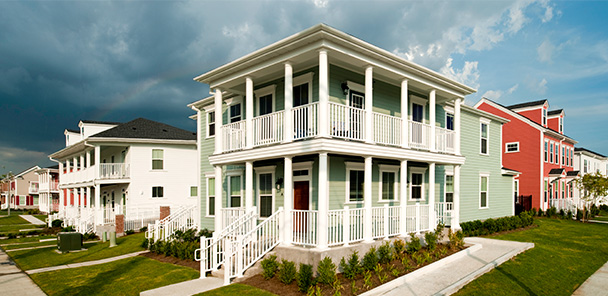 Exterior of a two-story, light green building with white, wrap-around front porches and lawn.